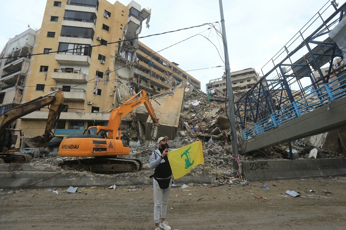 Un partidario de Hezbollah sostiene la bandera amarilla del grupo militante libanés frente a la destrucción en Beirut.