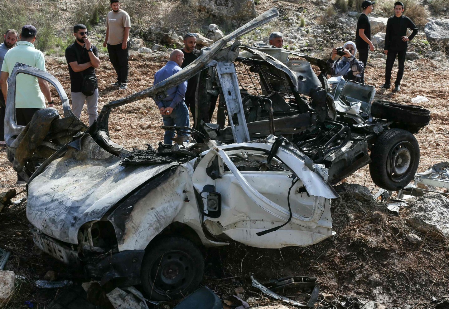 Personas inspeccionan los restos de un vehículo destruido por un ataque israelí en Haruf, sur de Líbano, con daños visibles en la zona.