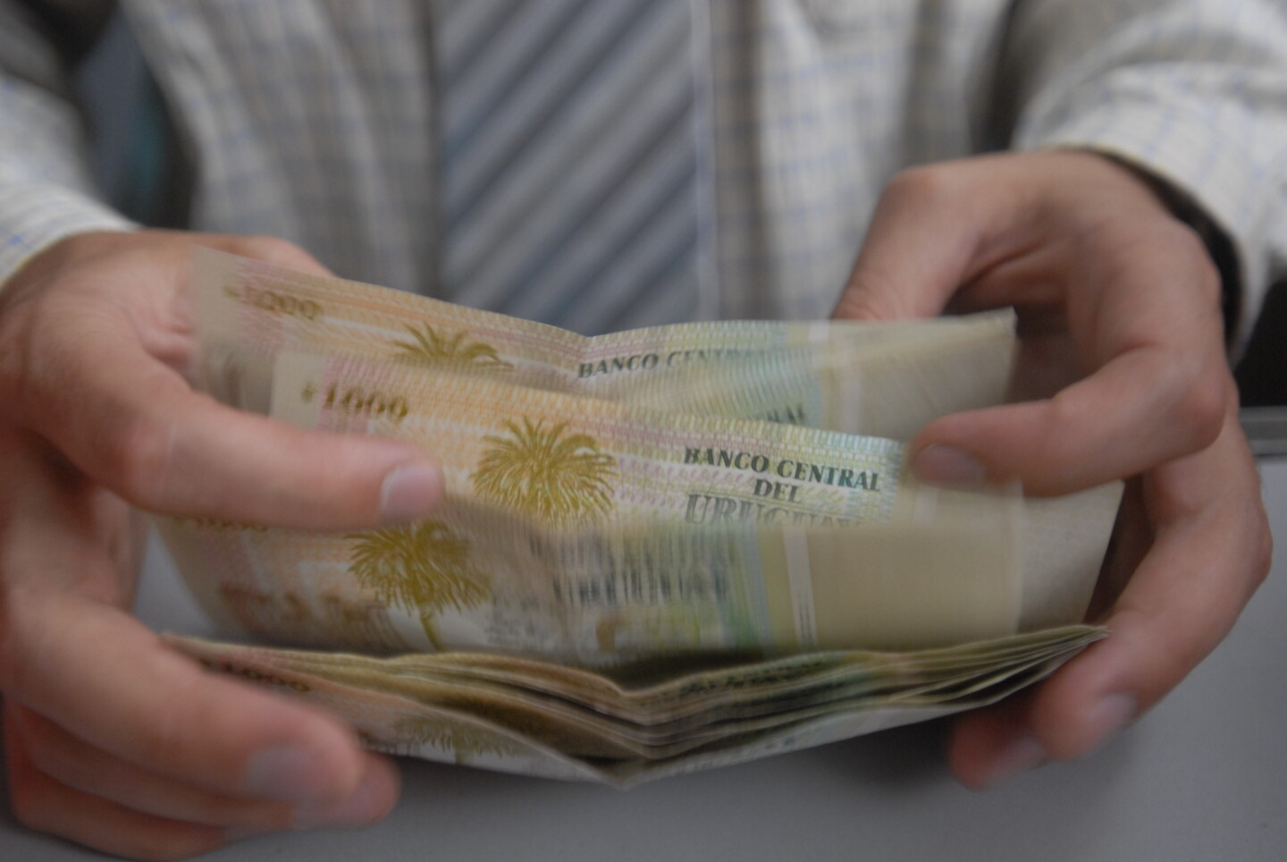 Persona contando billetes de mil pesos uruguayos.