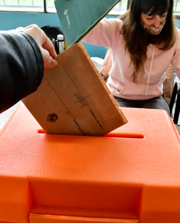 Mujer coloca su voto dentro de una urna naranja.