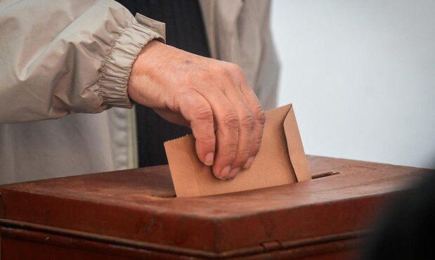 Hombre deposita sobre con su votación en una urna.