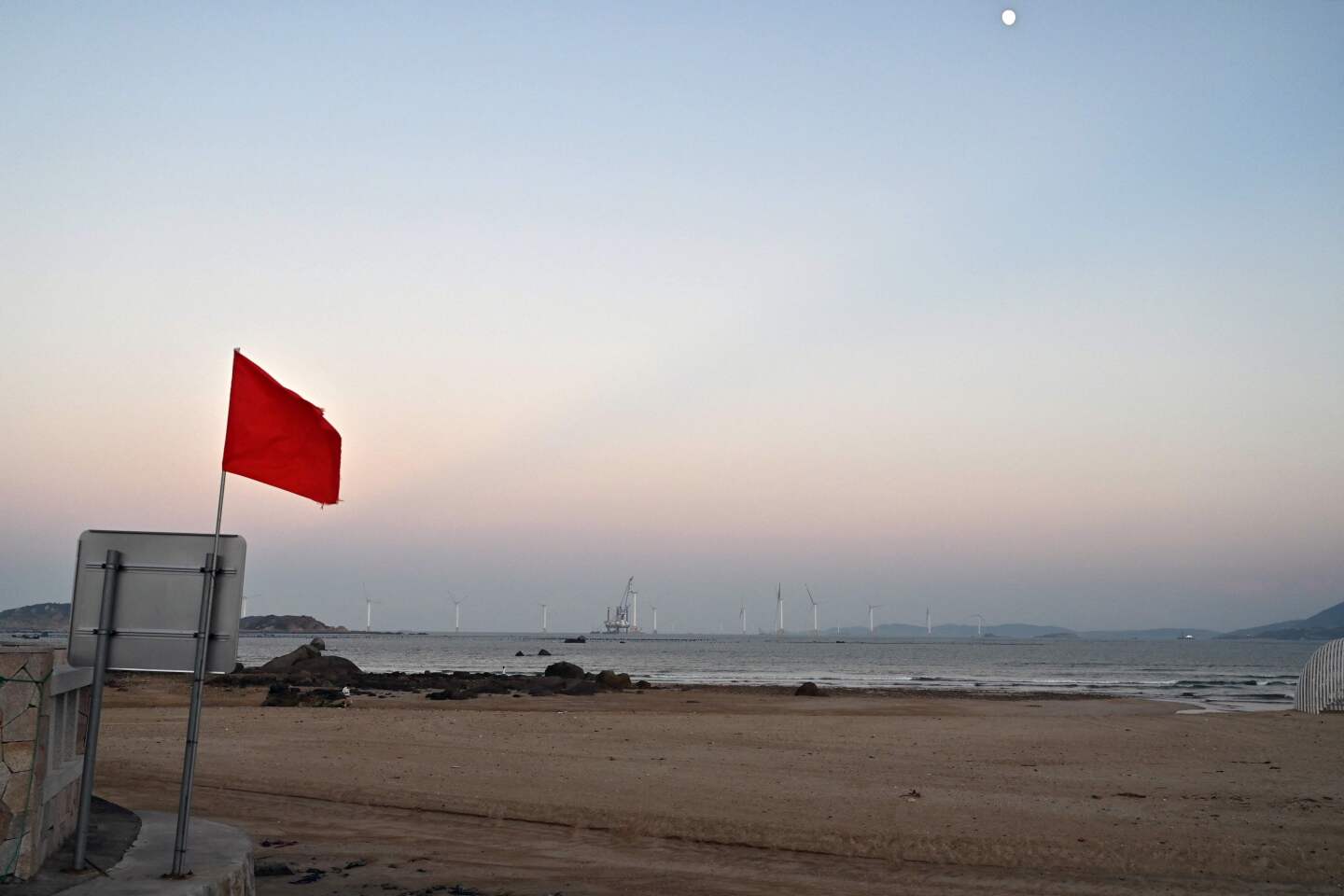 Turbinas eólicas (al fondo) más allá de una bandera roja en una playa de la isla Pingtan, el punto más cercano en China a la isla principal de Taiwán