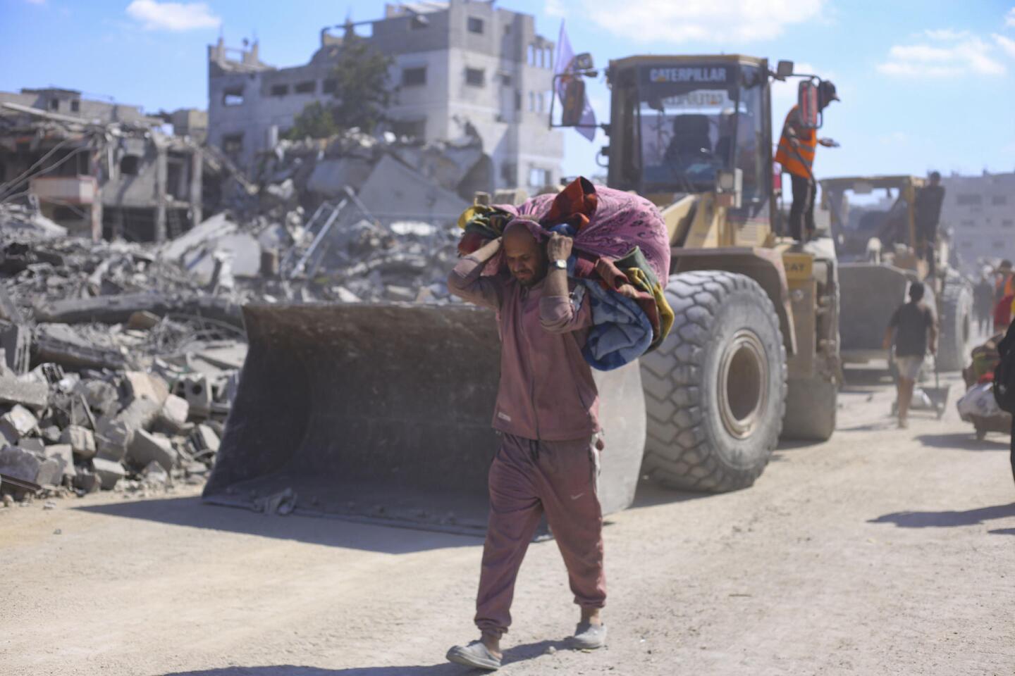 Un hombre con una bolsa con sus pertenencias pasa ante varias excavadoras del Ayuntamiento de la ciudad de Gaza que comienza este martes las operaciones de remoción de escombros y apertura de las calles principales de la capital gazatí.