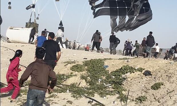 Palestinos corren hacia paracaídas sujetos a paquetes de alimentos.