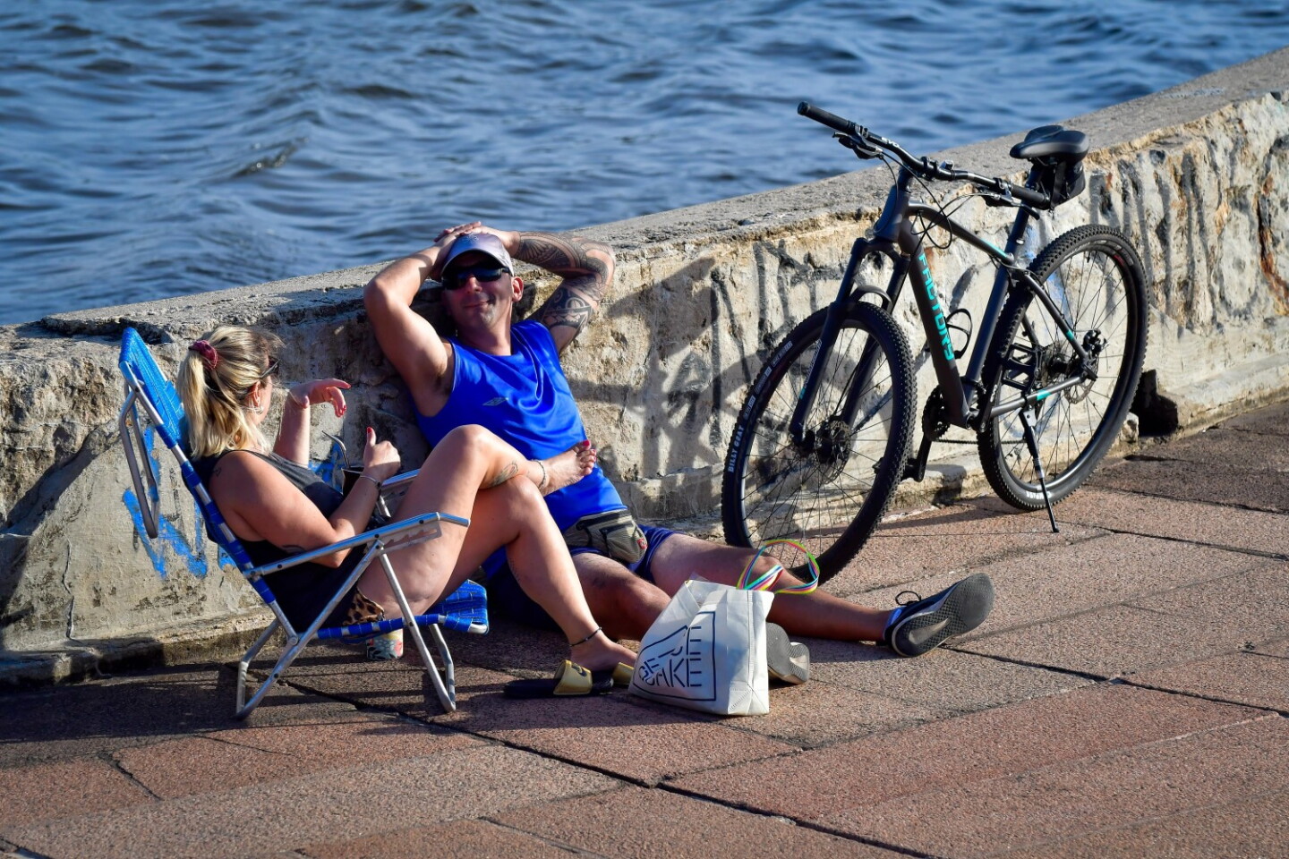 Personas sentadas en la rambla de Montevideo en un día de calor.