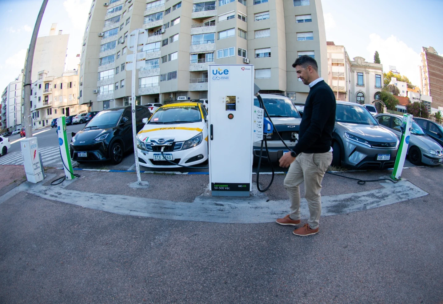 Hombre camina frente a un cargador de autos eléctricos de la vía pública