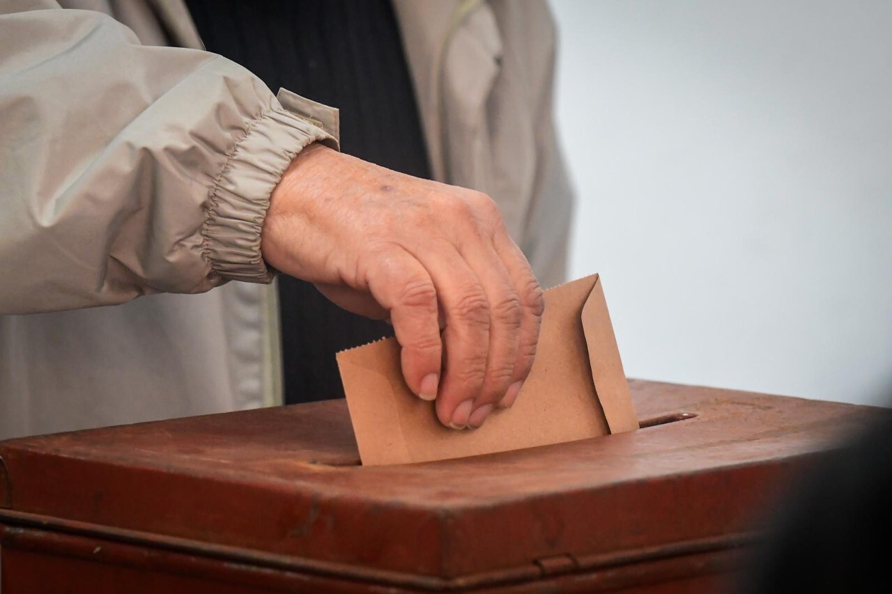 Hombre deposita sobre con su votación en una urna.