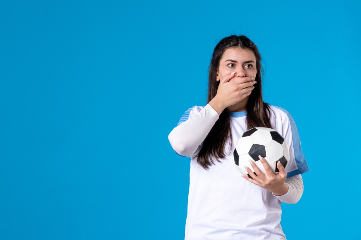 Mujer se tapa la boca mientras sostiene una pelota de fútbol.