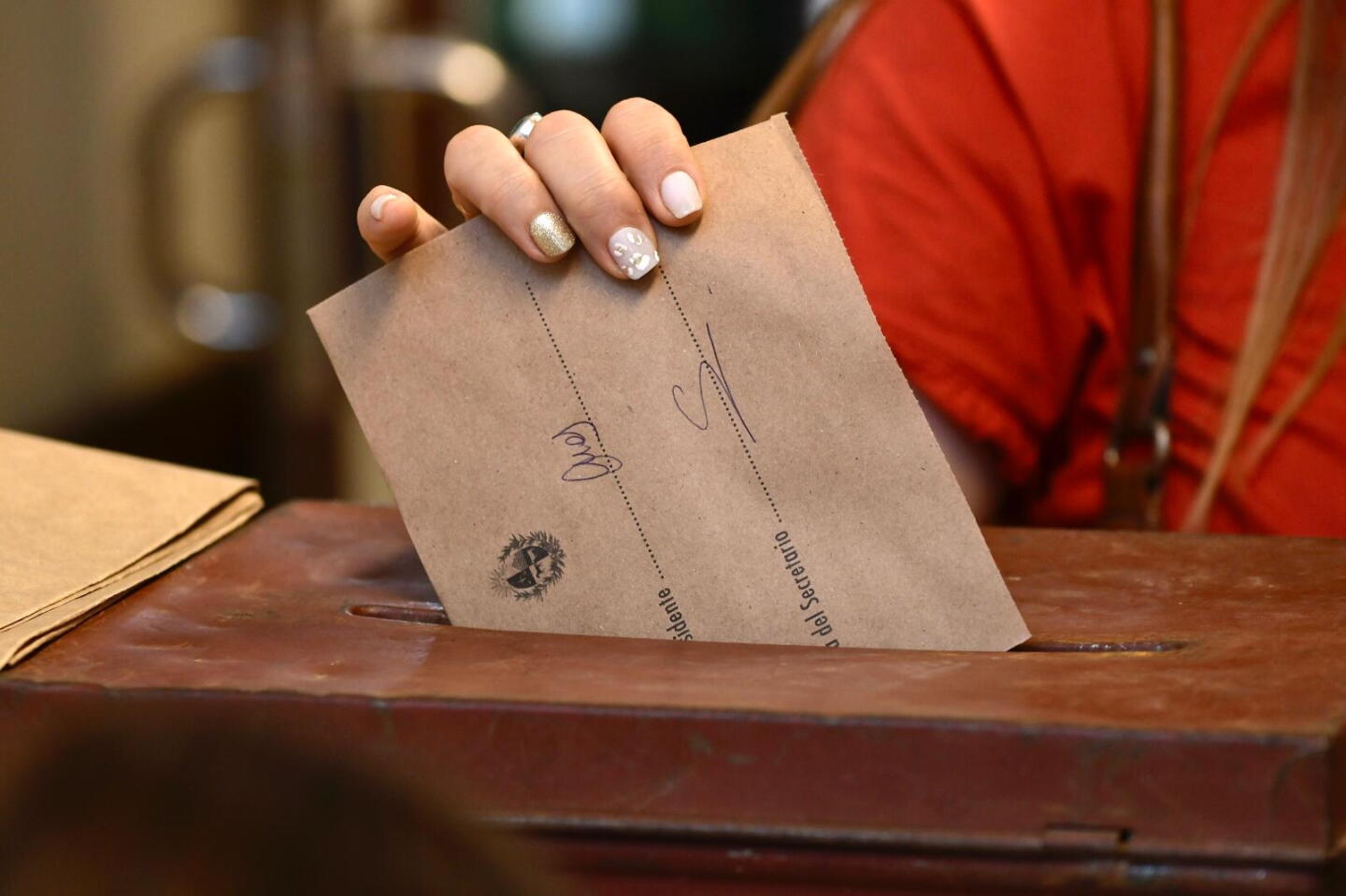 Una mujer introduciendo un sobre de votación en una urna.
