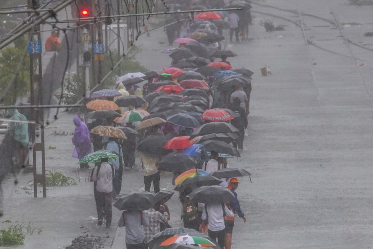 Personas caminan sobre las vías del tren anegadas durante fuertes lluvias en Vasai, en las afueras de Bombay (India)